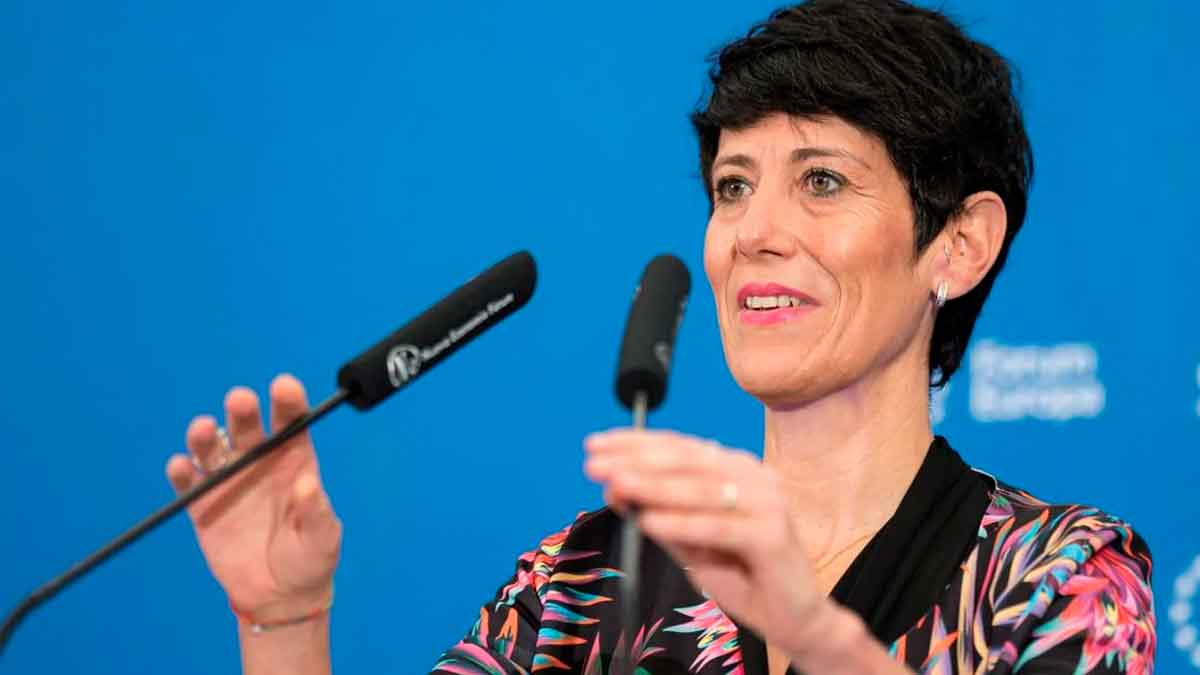 Elma Saiz explica la compatibilidad entre paro y jubilación durante una rueda de prensa, con micrófonos y fondo azul