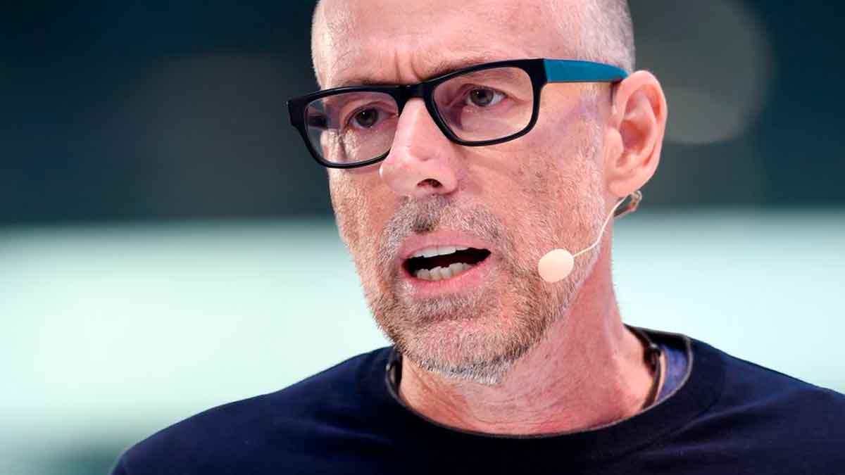 Primer plano de un profesor universitario con gafas y micrófono mientras expone su propuesta de suprimir pensiones a jubilados adinerados