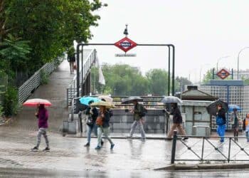 Personas con paraguas en la entrada del metro Miguel Hernández de Madrid durante una jornada de lluvias débiles