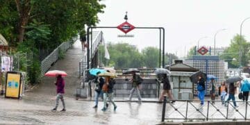 Personas con paraguas en la entrada del metro Miguel Hernández de Madrid durante una jornada de lluvias débiles