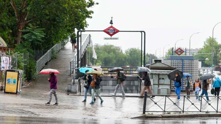Personas con paraguas en la entrada del metro Miguel Hernández de Madrid durante una jornada de lluvias débiles