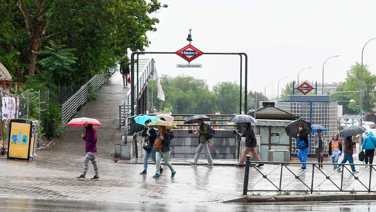 Personas con paraguas en la entrada del metro Miguel Hernández de Madrid durante una jornada de lluvias débiles