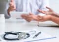 Consulta médica con doctor y paciente; un estetoscopio sobre documentos simboliza la baja que resta meses de paro según el SEPE