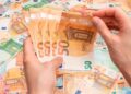 Manos contando billetes de 50 € ilustran el pago único de 37.800 € del SEPE para emprender