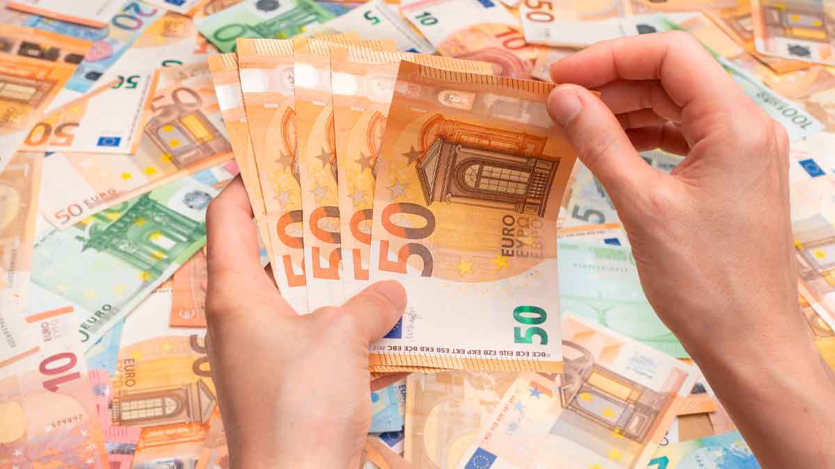Manos contando billetes de 50 € ilustran el pago único de 37.800 € del SEPE para emprender
