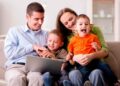 Padres con sus dos hijos usando un portátil para solicitar las becas de Educación Infantil de la Comunidad de Madrid