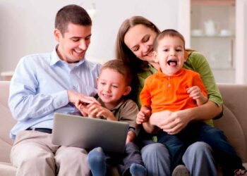 Padres con sus dos hijos usando un portátil para solicitar las becas de Educación Infantil de la Comunidad de Madrid