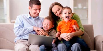 Padres con sus dos hijos usando un portátil para solicitar las becas de Educación Infantil de la Comunidad de Madrid