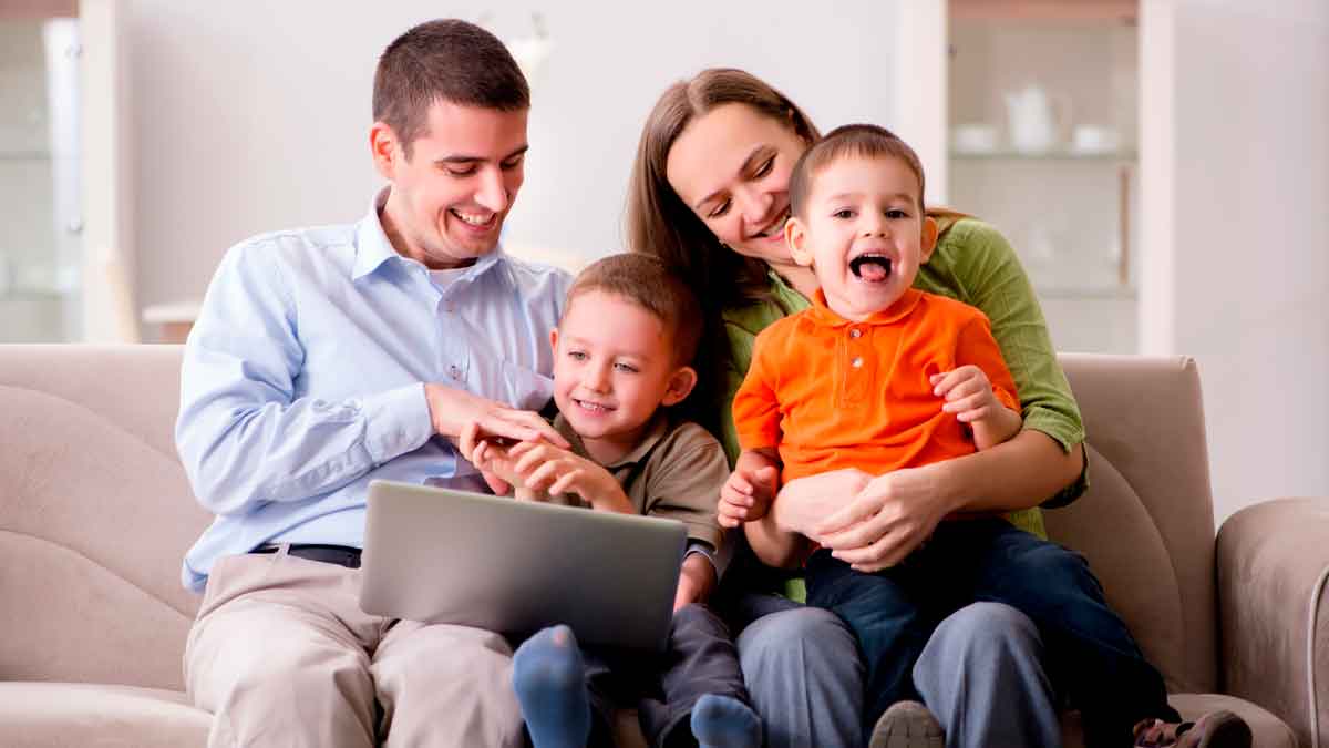 Padres con sus dos hijos usando un portátil para solicitar las becas de Educación Infantil de la Comunidad de Madrid