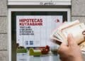Ayudas para pagar la hipoteca 2025: anuncio de hipotecas Kutxabank y mano con billetes de euro.