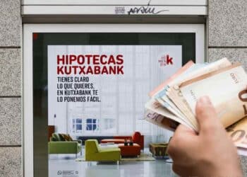 Ayudas para pagar la hipoteca 2025: anuncio de hipotecas Kutxabank y mano con billetes de euro.