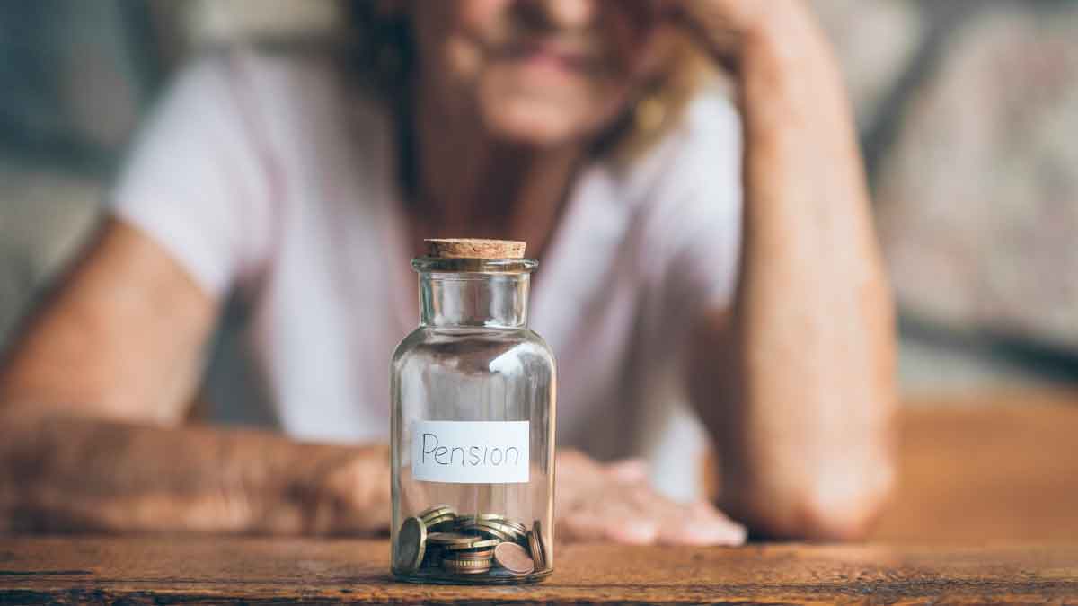 Tarro de cristal con monedas y la palabra “pensión” delante de una mujer mayor pensativa, símbolo del ahorro para jubilarse en 2026 con 15 años cotizados