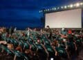 Espectadores en sillas reclinables ante pantalla gigante durante un cine de verano gratis en parque de Madrid al anochecer.