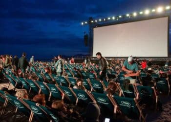 Espectadores en sillas reclinables ante pantalla gigante durante un cine de verano gratis en parque de Madrid al anochecer.