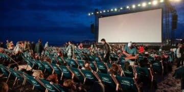Espectadores en sillas reclinables ante pantalla gigante durante un cine de verano gratis en parque de Madrid al anochecer.