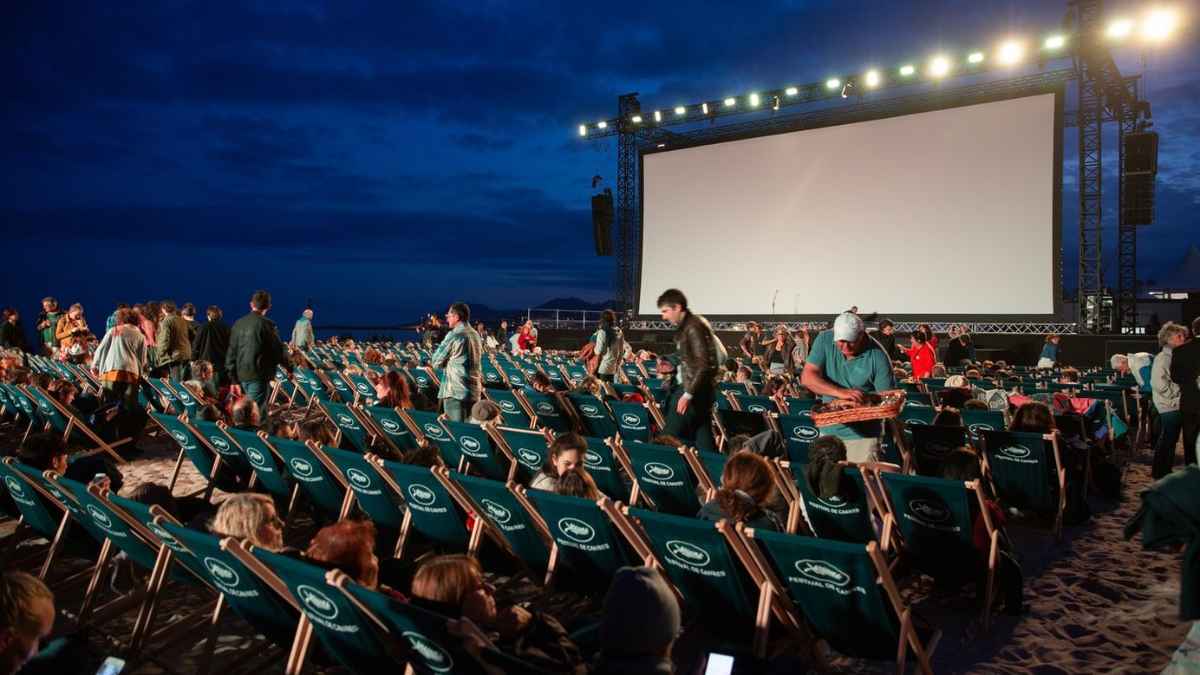 Espectadores en sillas reclinables ante pantalla gigante durante un cine de verano gratis en parque de Madrid al anochecer.