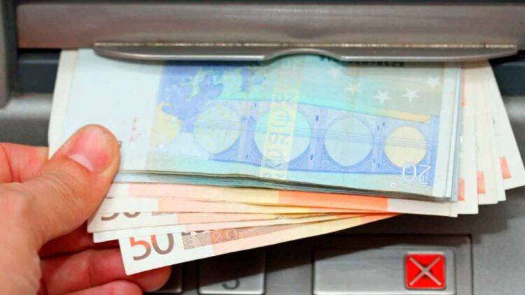 Mano retirando billetes de 20 y 50 € en cajero, símbolo del cobro del paro de junio 2025 adelantado por varios bancos
