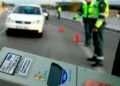 Dispositivo de etilómetro en primer plano con agentes de la Guardia Civil y conos señalizando un control de alcoholemia en carretera