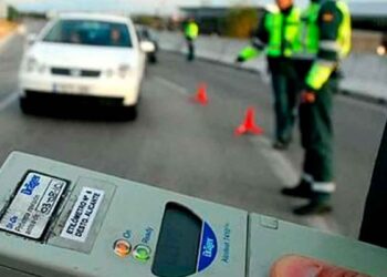 Dispositivo de etilómetro en primer plano con agentes de la Guardia Civil y conos señalizando un control de alcoholemia en carretera