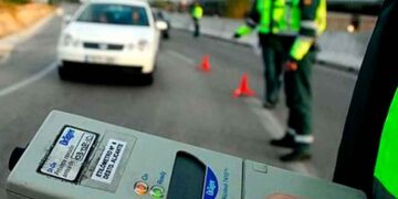 Dispositivo de etilómetro en primer plano con agentes de la Guardia Civil y conos señalizando un control de alcoholemia en carretera