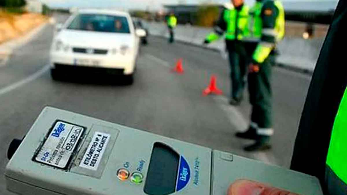 Dispositivo de etilómetro en primer plano con agentes de la Guardia Civil y conos señalizando un control de alcoholemia en carretera