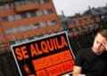 Hombre preocupado junto a cartel “Se alquila piso nuevo” por impuesto del 2 % a no residentes en España.