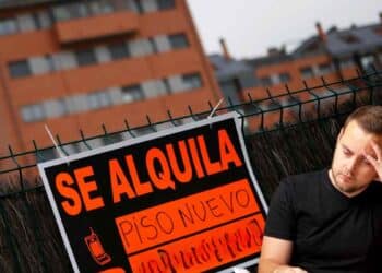 Hombre preocupado junto a cartel “Se alquila piso nuevo” por impuesto del 2 % a no residentes en España.