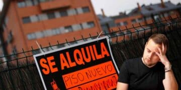Hombre preocupado junto a cartel “Se alquila piso nuevo” por impuesto del 2 % a no residentes en España.