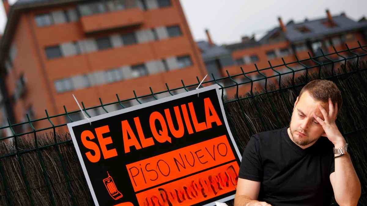 Hombre preocupado junto a cartel “Se alquila piso nuevo” por impuesto del 2 % a no residentes en España.