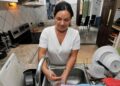 Empleada del hogar lavando platos en la cocina mientras realiza su jornada laboral doméstica a tiempo completo