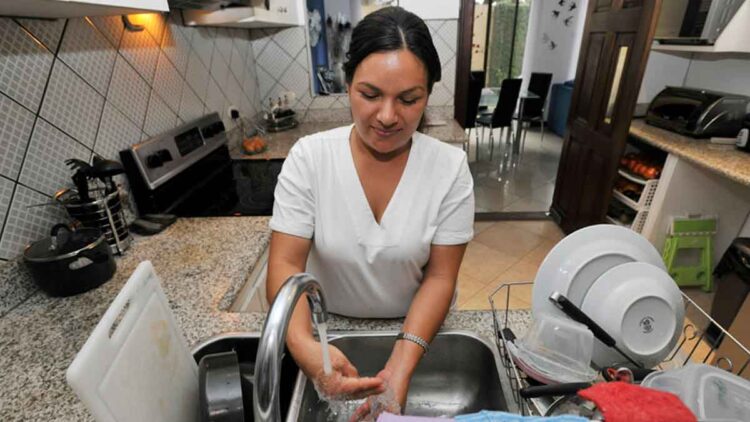 Empleada del hogar lavando platos en la cocina mientras realiza su jornada laboral doméstica a tiempo completo