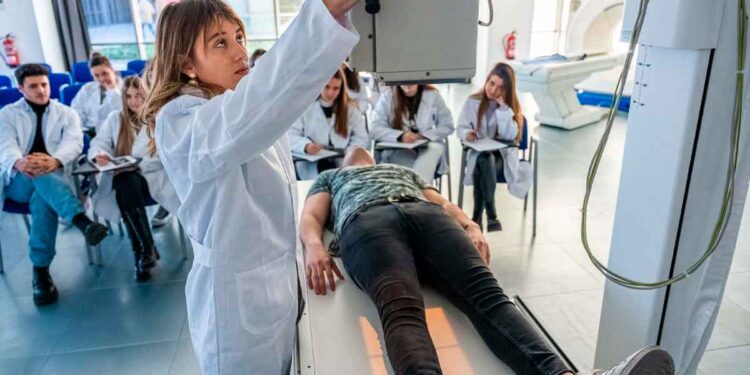 Profesora de FP Sanitaria ajusta equipo de rayos X mientras el alumnado observa la práctica clínica en Madrid, curso 2025-26