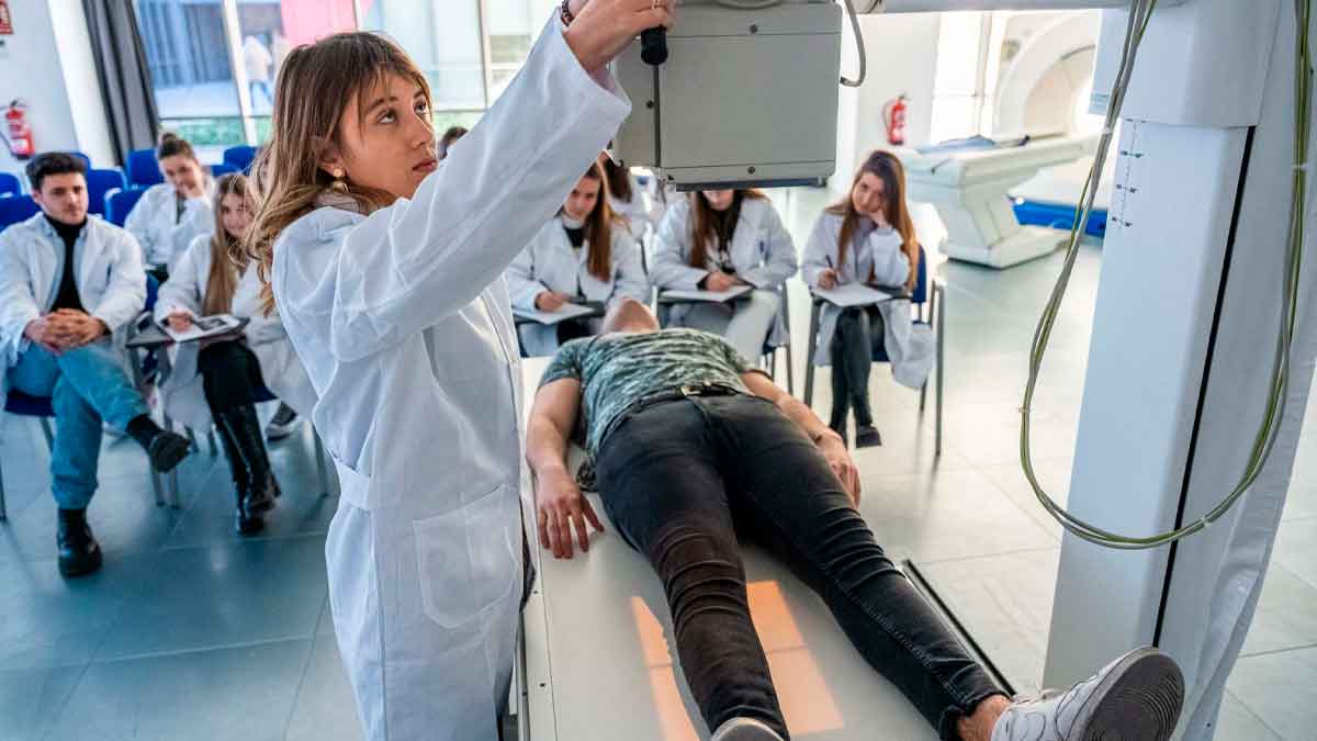 Profesora de FP Sanitaria ajusta equipo de rayos X mientras el alumnado observa la práctica clínica en Madrid, curso 2025-26