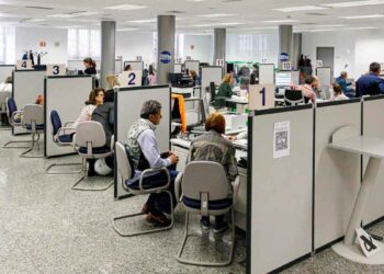 Personas siendo atendidas en cubículos numerados de la Agencia Tributaria para presentar la declaración presencial de la Renta 2024/25