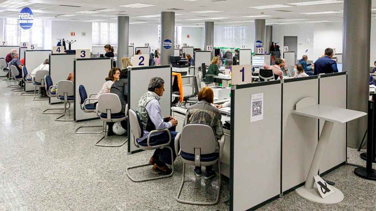 Personas siendo atendidas en cubículos numerados de la Agencia Tributaria para presentar la declaración presencial de la Renta 2024/25