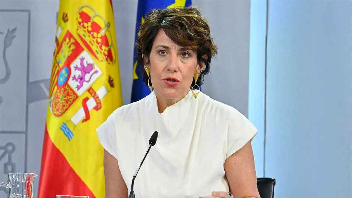 Elma Saiz en rueda de prensa anuncia la jubilación anticipada sin recortes desde los 52 años, con bandera nacional al fondo