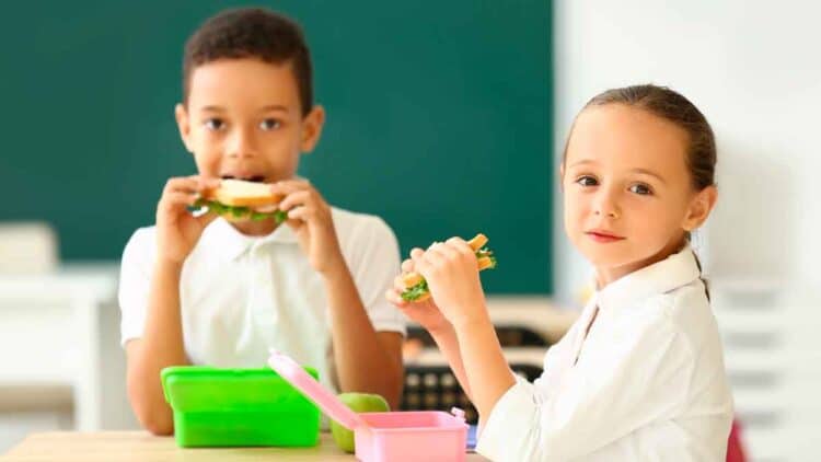 Dos escolares comen bocadillos en clase gracias al programa de desayunos gratuitos de Madrid 2025-2026