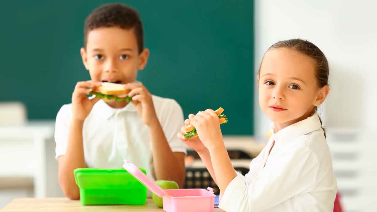 Dos escolares comen bocadillos en clase gracias al programa de desayunos gratuitos de Madrid 2025-2026