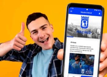 Joven sonriente muestra la app madrid móvil en su smartphone para gestionar trámites del ayuntamiento