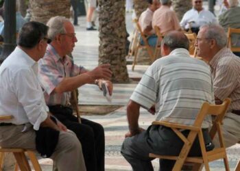 Grupo de jubilados sentados y conversando en una plaza arbolada de España