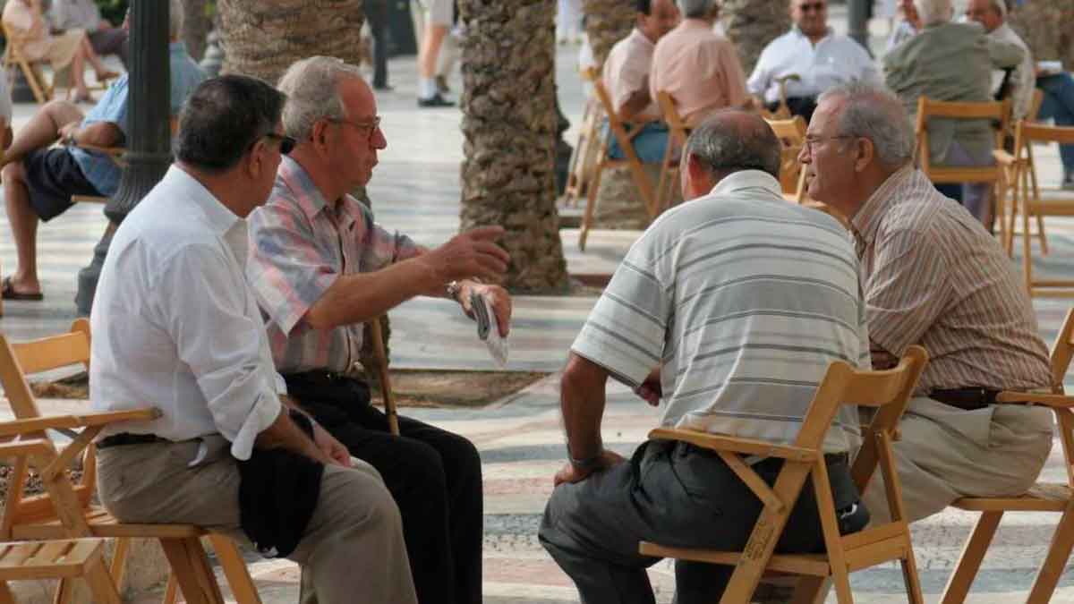 Grupo de jubilados sentados y conversando en una plaza arbolada de España