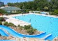 Piscina pública al aire libre en Madrid con tobogán azul y bañistas, tarifas más caras para no empadronados.