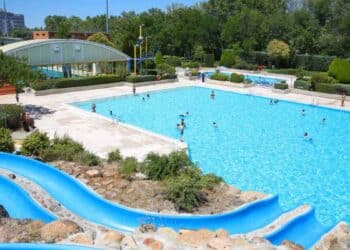 Piscina pública al aire libre en Madrid con tobogán azul y bañistas, tarifas más caras para no empadronados.