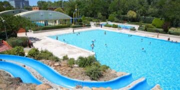 Piscina pública al aire libre en Madrid con tobogán azul y bañistas, tarifas más caras para no empadronados.