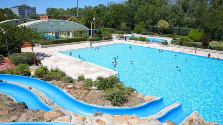 Piscina pública al aire libre en Madrid con tobogán azul y bañistas, tarifas más caras para no empadronados.