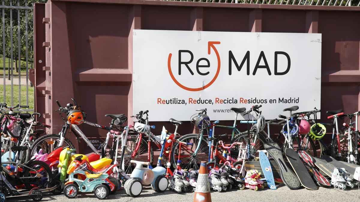 Bicicletas, patinetes y monopatines ante el cartel de ReMAD en un punto limpio de Madrid listos para su reutilización.