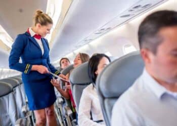 tripulante de cabina atendiendo a pasajeros en el pasillo de un avión, ejemplo del trabajo y sueldo de un TCP en España 2025.