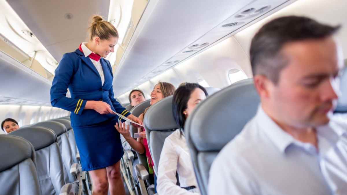 tripulante de cabina atendiendo a pasajeros en el pasillo de un avión, ejemplo del trabajo y sueldo de un TCP en España 2025.