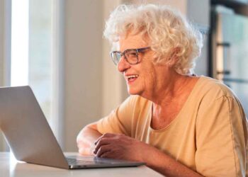 Mujer mayor de 65 años sonríe frente a un portátil mientras realiza online los trámites gratuitos disponibles en 2025
