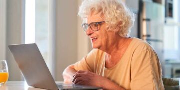 Mujer mayor de 65 años sonríe frente a un portátil mientras realiza online los trámites gratuitos disponibles en 2025